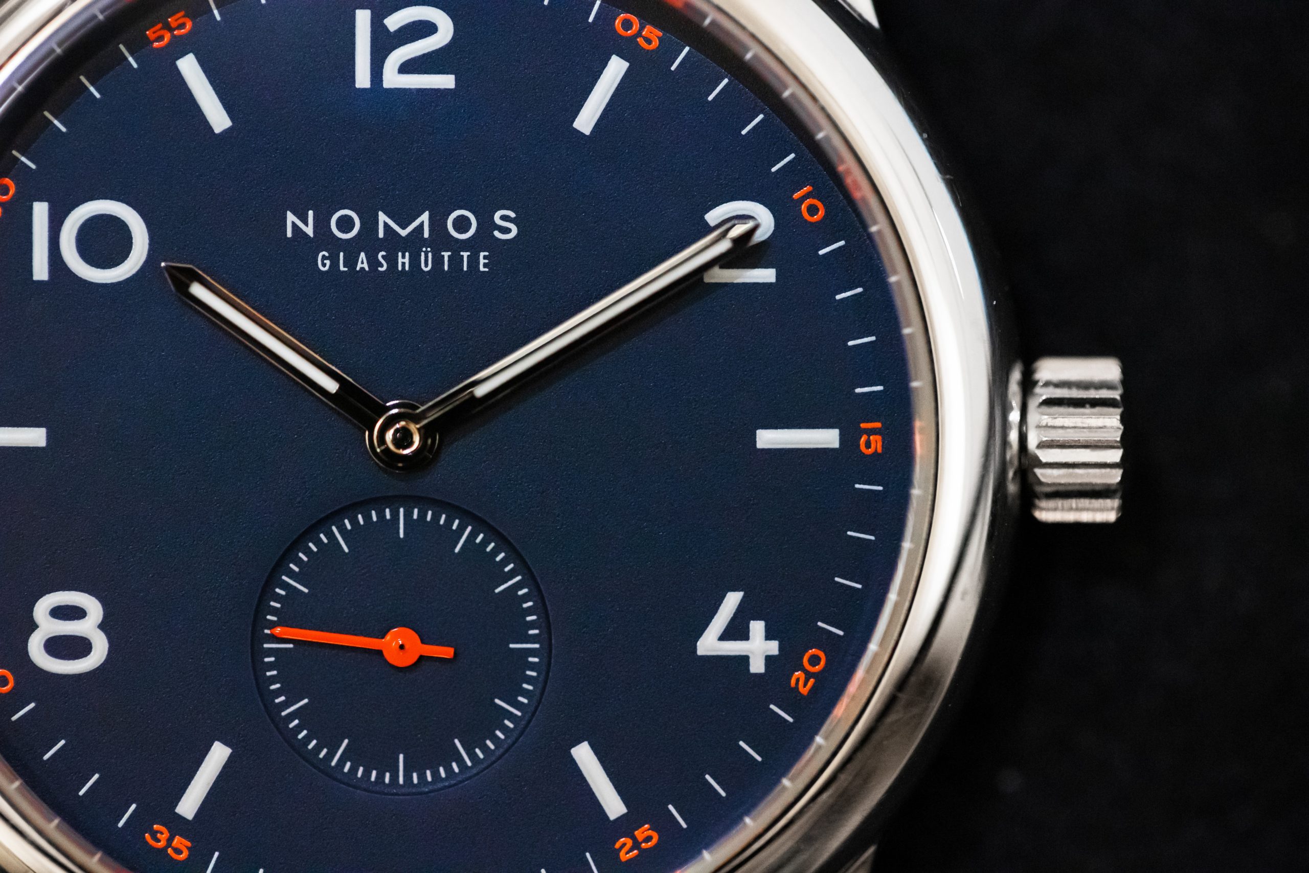 The watch is a Nomos Glashütte with a blue dial and orange accents. The watch is a Nomos Glashütte with a blue dial and orange accents.