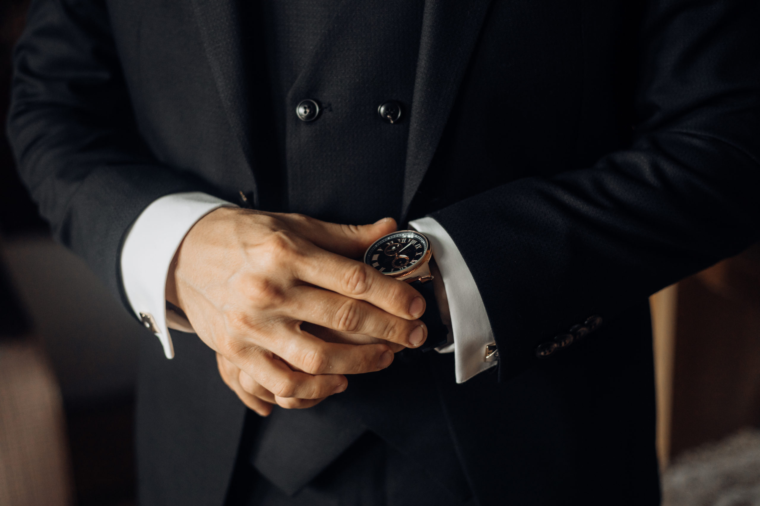 A man wearing a black suit and a gold watch. A man wearing a black suit and a gold watch.